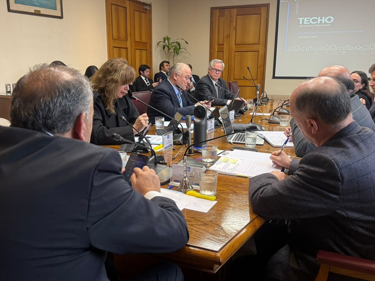 Panorámica de la sala de la Comisión de Vivienda y Urbanismo del Senado durante la exposición de TECHO-Chile, con la presentación proyectada al fondo.